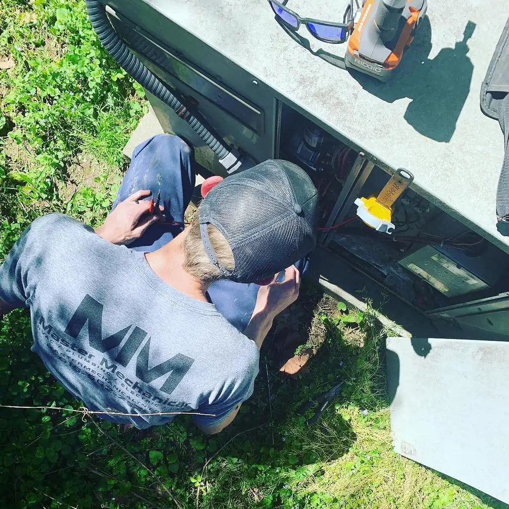 Master Mechanical technician in an MM logo shirt working inside the control box of an outdoor unit