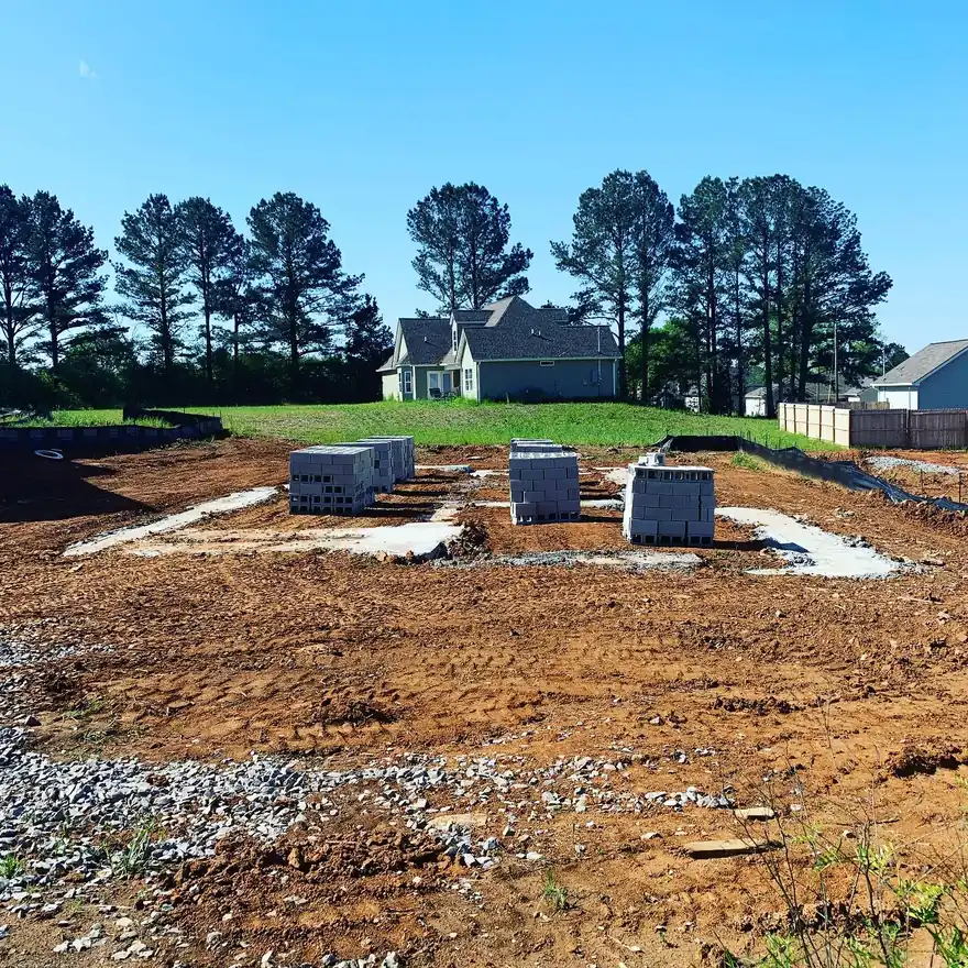 New-construction lot in Middle Tennessee with block stacks on the footings and a finished house behind