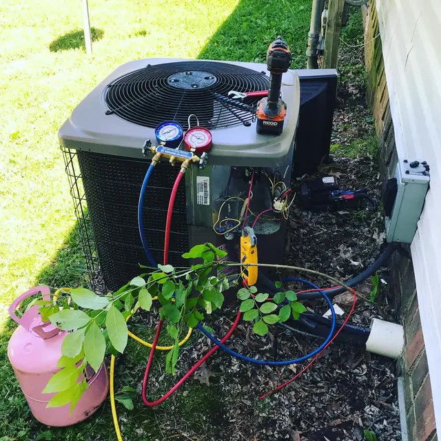 Manifold gauges and hoses on a residential condenser beside a refrigerant cylinder